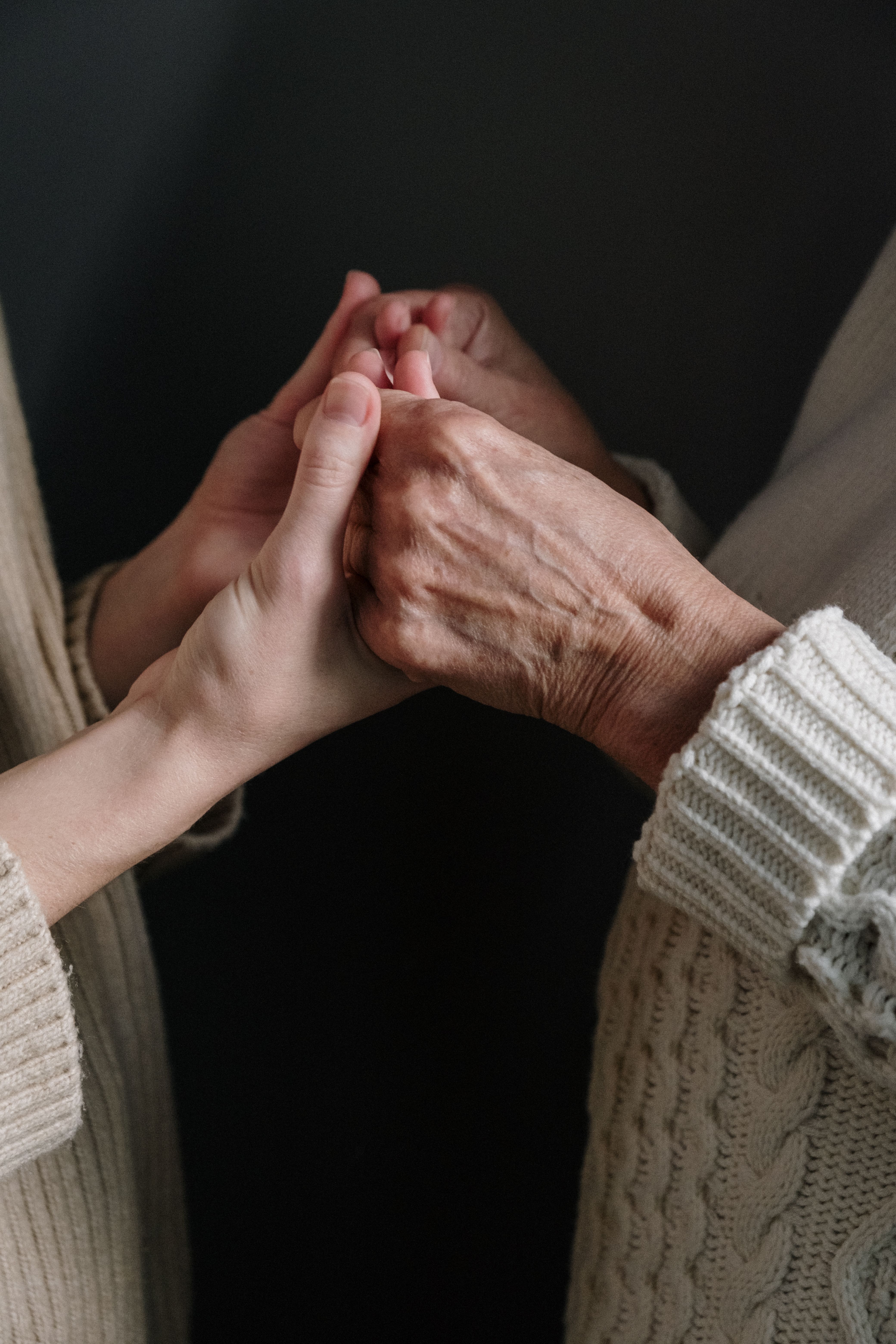 Close-up of a younger hand gently holding an older adult's hand
