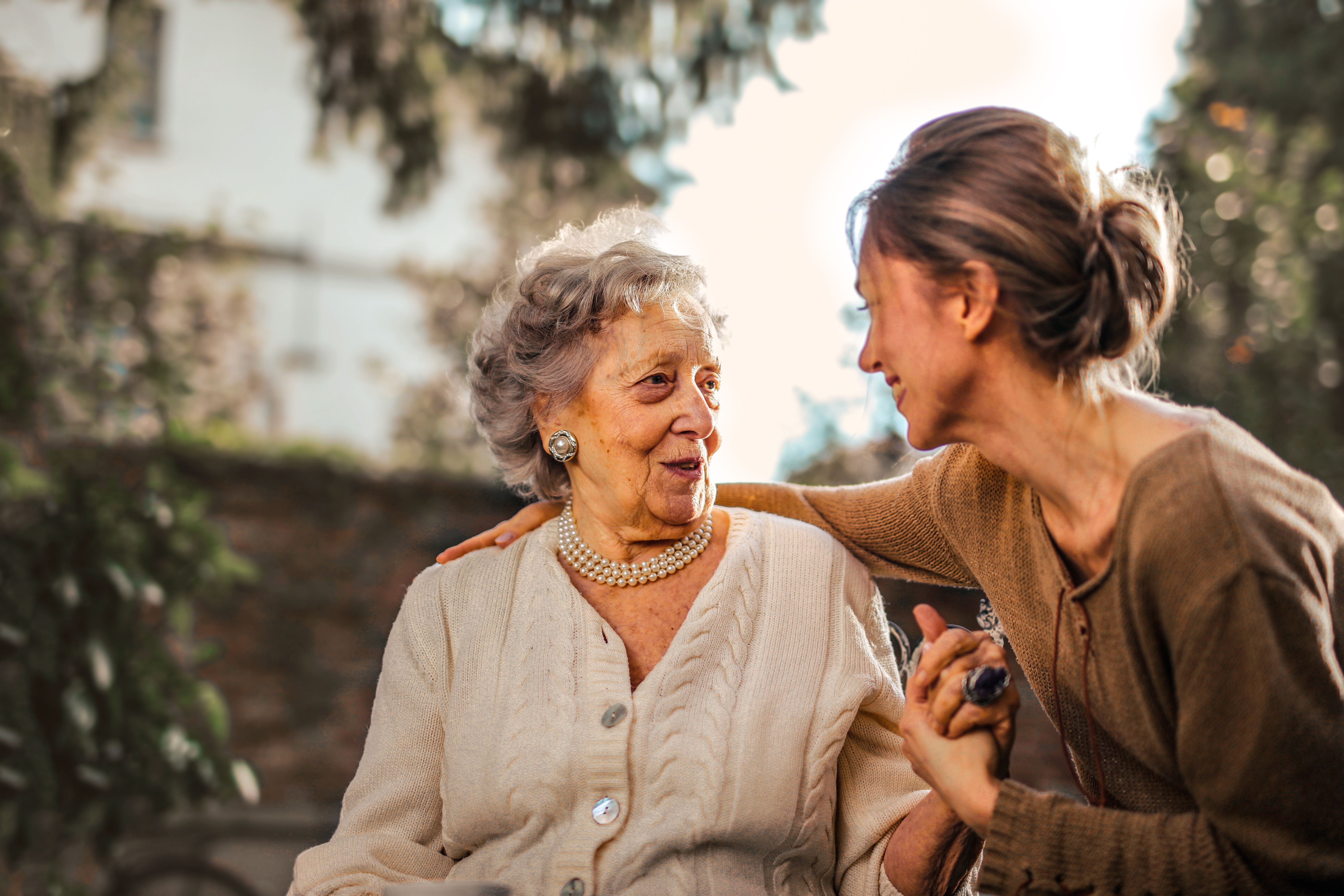 An older woman and a younger caregiver sharing a warm, affectionate moment together outdoors